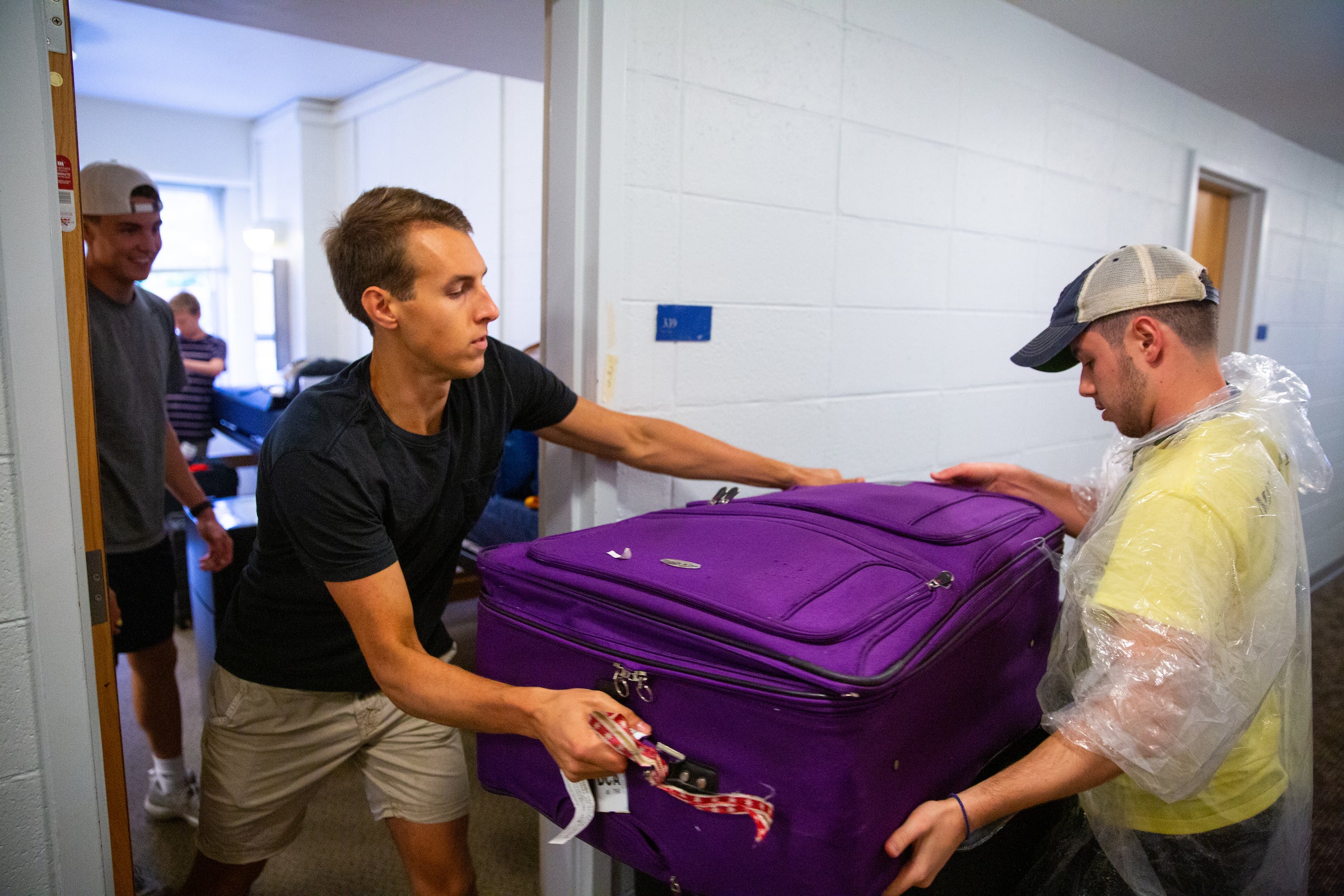 two men passing a suitcase out of a dorm room