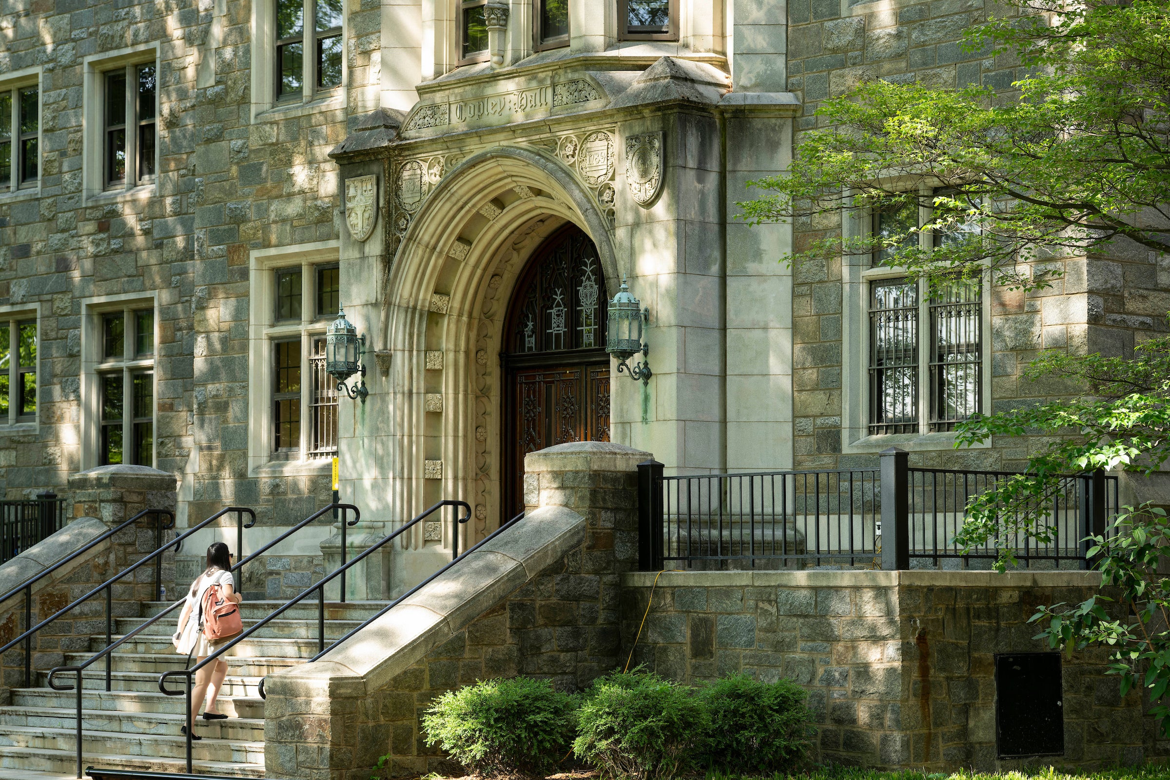 stone building with a wooden, arched door. There is a staircase entrance with a student walking up.