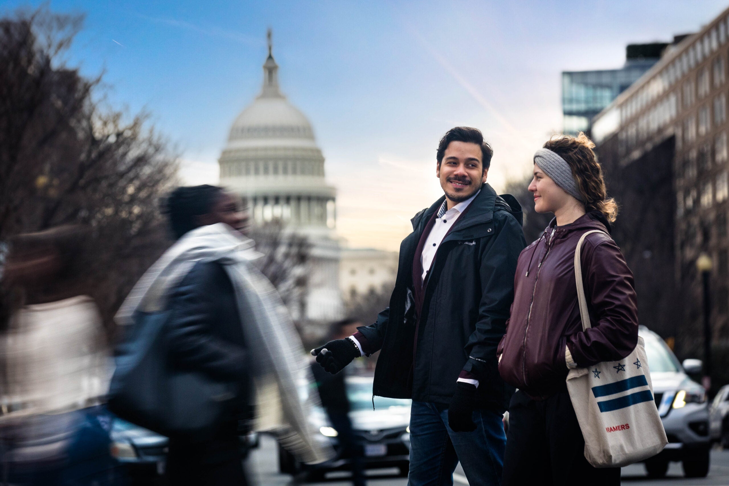students cross the street in conversation. View of US Capitol in the background. 