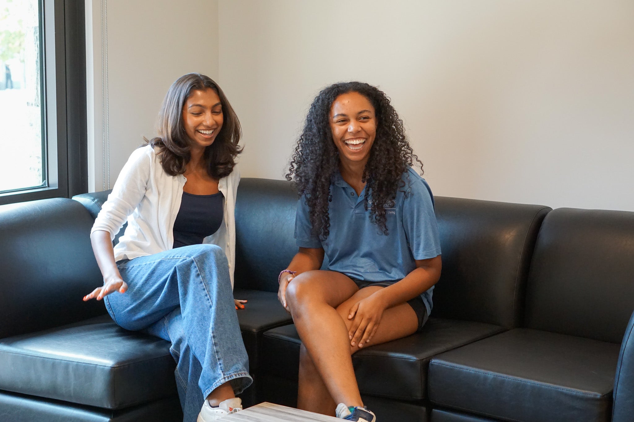 Two students laugh together on a couch in the living area of their on-campus suite.